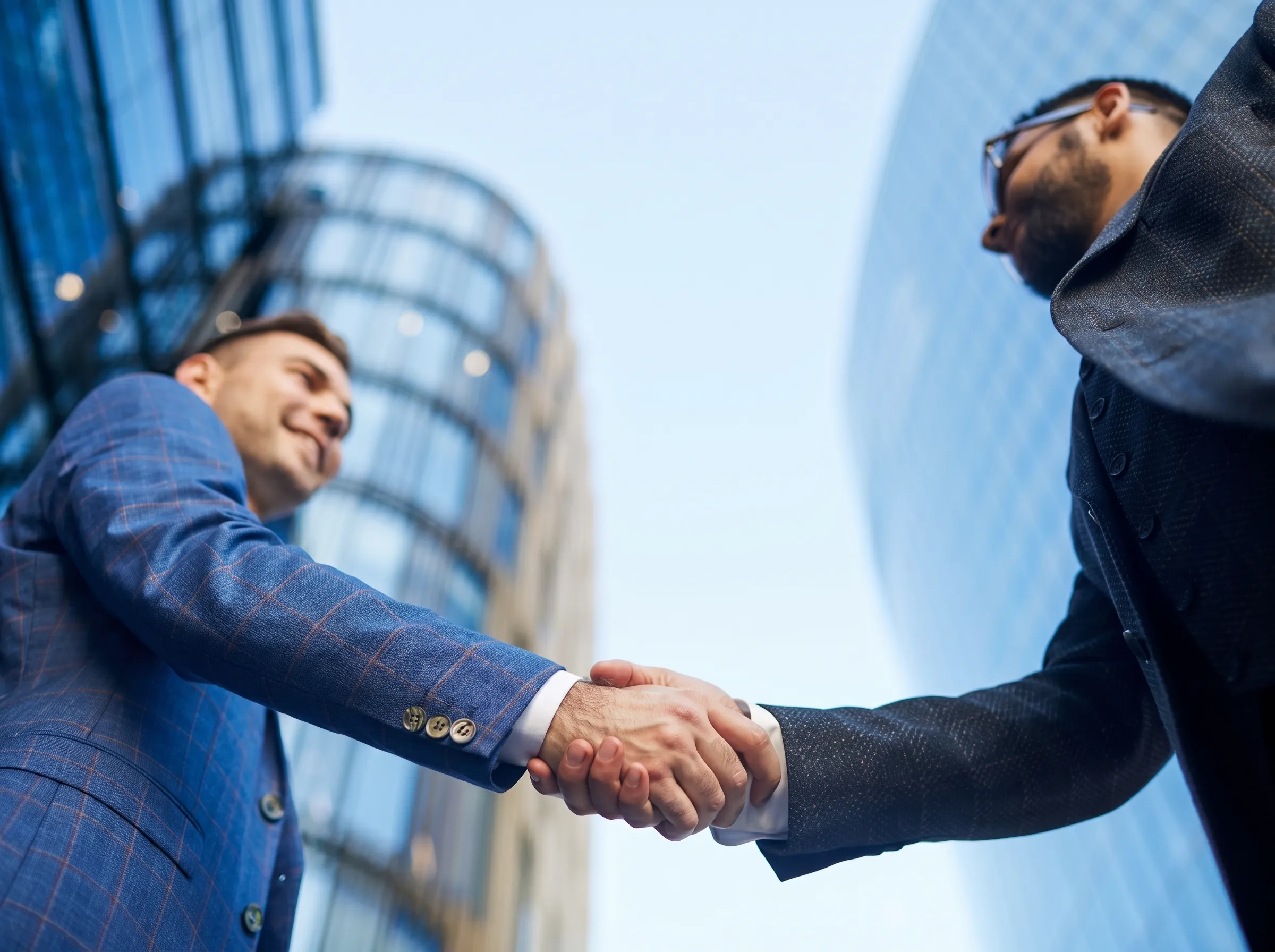 Two businessmen shaking hands outside corporate office buildings